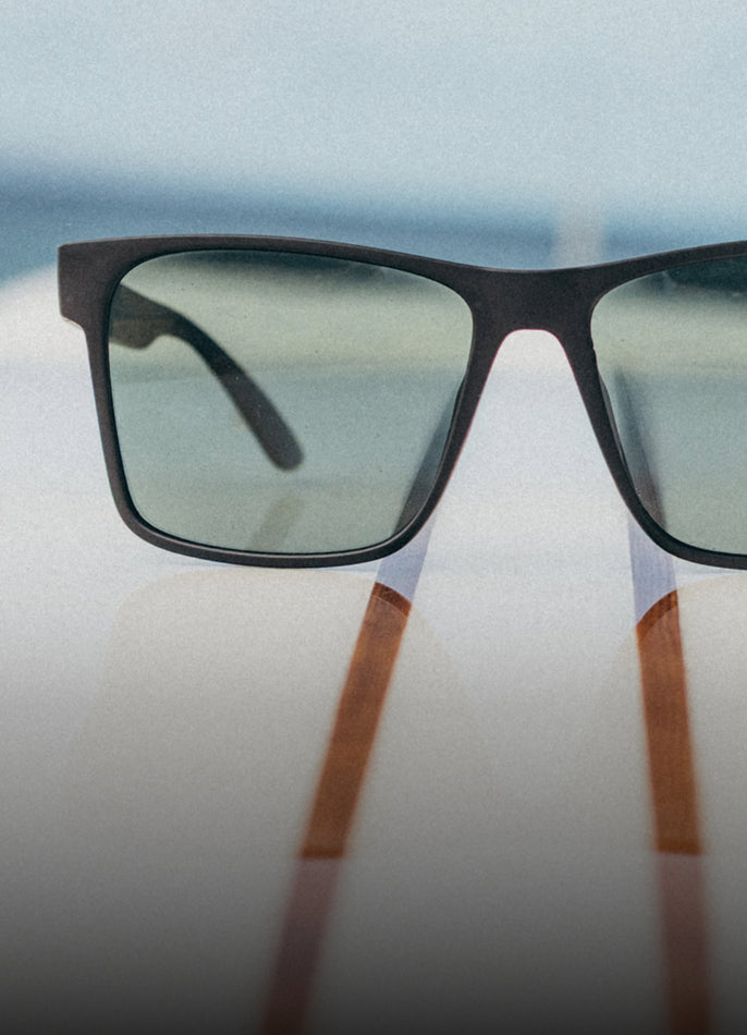Sunglasses with black frames and brown accents on a reflective surface with a blurred background