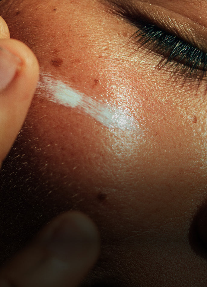 Close-up of a hand applying white cream to a person's face