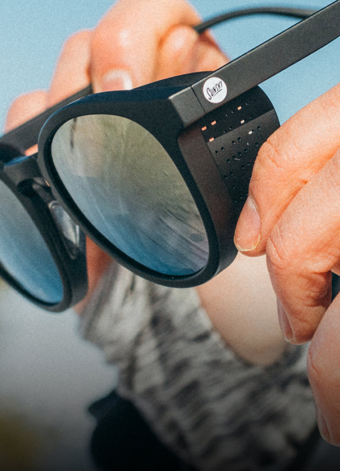 Close-up of a person holding a pair of black sunglasses with a brand logo.