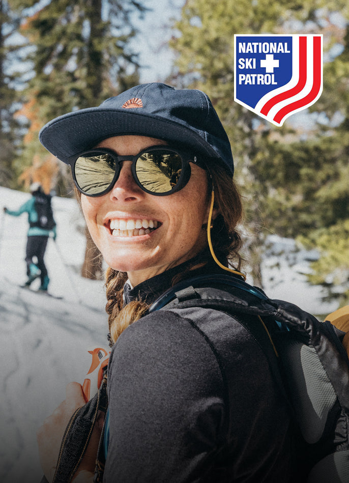 Person wearing sunglasses and a cap with National Ski Patrol logo in a snowy background