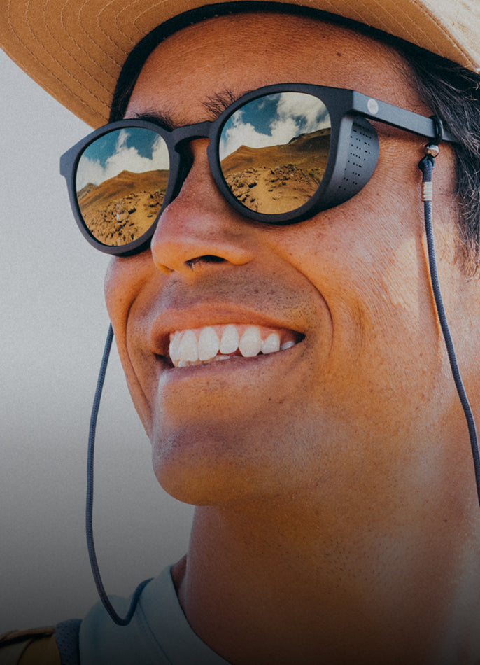 Person wearing sunglasses with desert landscape reflection, smiling outdoors.