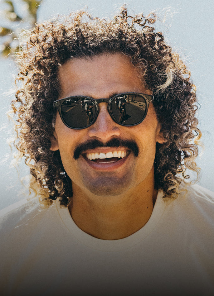 Man with sunglasses and curly hair against a blurred natural background