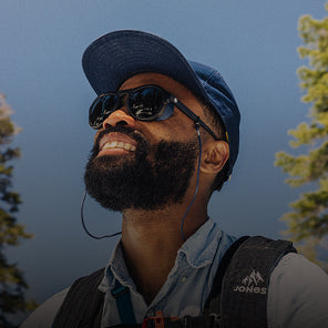Man wearing sunglasses and a cap with a backpack, looking up against a blue sky.