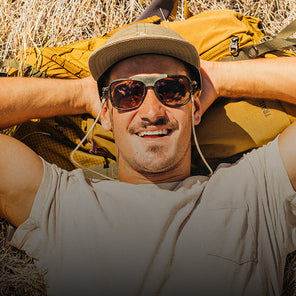Man with sunglasses and a backpack lying on the ground in a natural setting