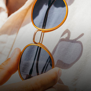 Gold-framed sunglasses held by a hand with a blurred background