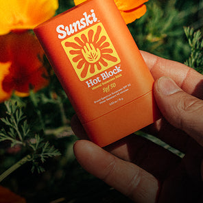 Hand holding a Sunsiki Sun Block stick with flowers in the background